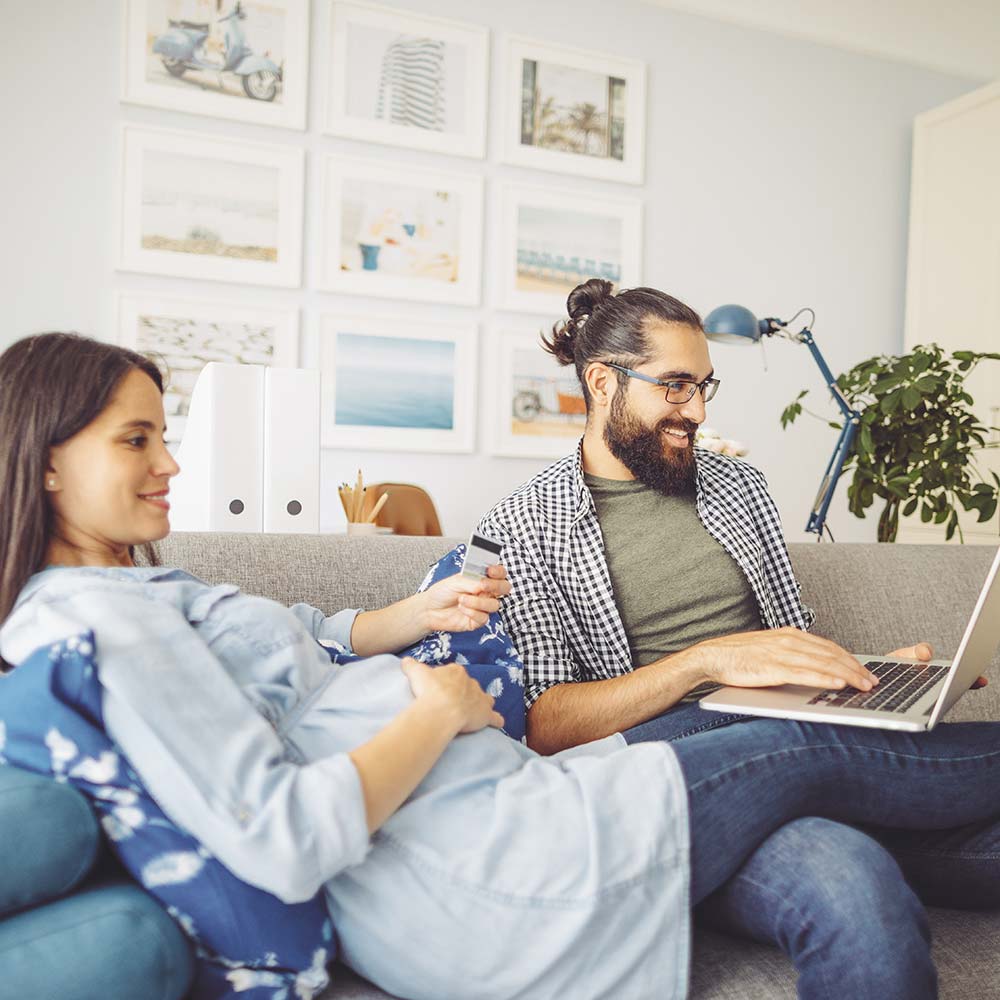 En gravid kvinna som sitter med sin man i soffan framför en laptop